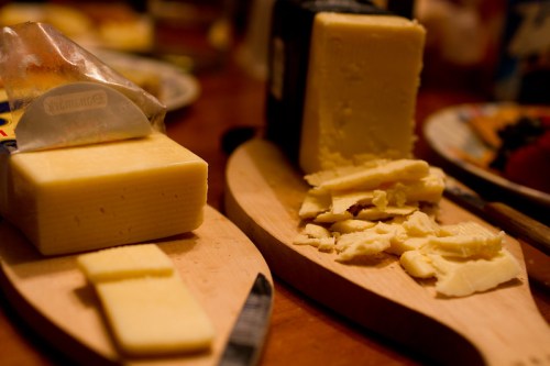 Two blocks of cheese on wooden boards, one partially sliced and the other crumbled, with knives nearby.