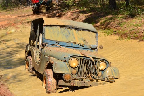 A muddy vintage jeep partially submerged in water, with a second vehicle visible in the background.