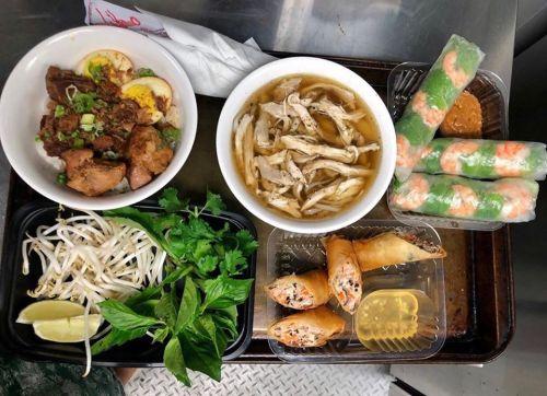 A tray of Vietnamese dishes including spring rolls, pho, herbs, bean sprouts, and dipping sauce.