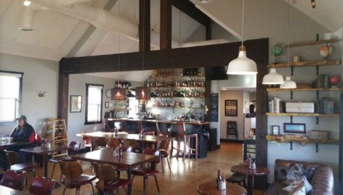 A cozy restaurant interior featuring wooden tables, a bar with shelves of bottles, and a warm, inviting atmosphere.