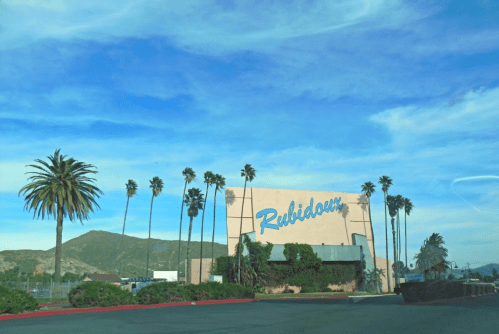 Sign for Rubidoux with palm trees and mountains in the background under a blue sky.