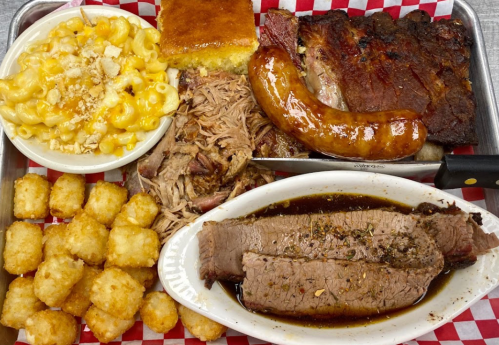 A tray of barbecue featuring brisket, pulled pork, sausage, macaroni and cheese, cornbread, and tater tots.