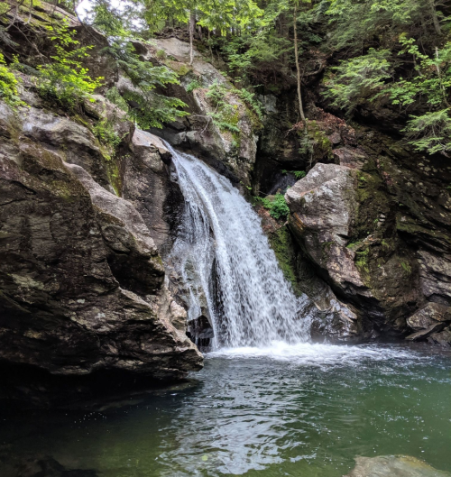 A serene waterfall cascading over rocky cliffs into a calm pool surrounded by lush greenery.