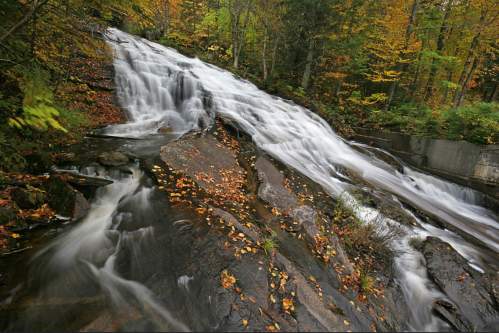A cascading waterfall flows over rocky terrain, surrounded by vibrant autumn foliage.