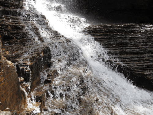 A cascading waterfall flows over rocky terrain, creating a misty spray in a natural setting.