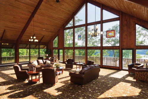 Spacious wooden lounge with large windows, comfortable seating, and scenic views of greenery outside.