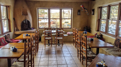Cozy restaurant interior with wooden tables, chairs, and large windows showcasing a natural view outside.