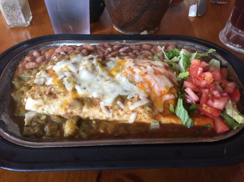 A sizzling plate of enchiladas topped with cheese, served with refried beans, lettuce, and diced tomatoes.