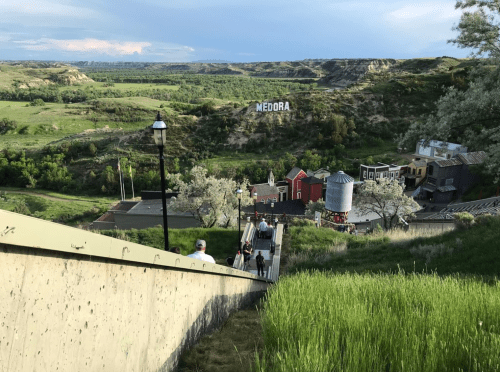 A view of Medora, North Dakota, from a hillside, showcasing buildings and greenery under a cloudy sky.