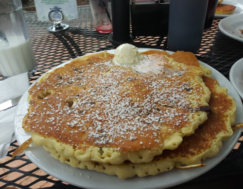 A plate of two large pancakes topped with powdered sugar and a dollop of butter, served on a black table.
