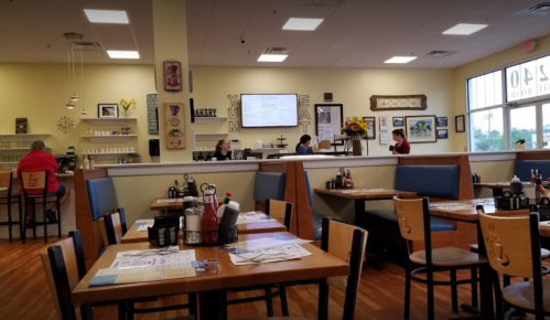 A cozy restaurant interior with wooden tables, blue seating, and staff serving customers at the counter.