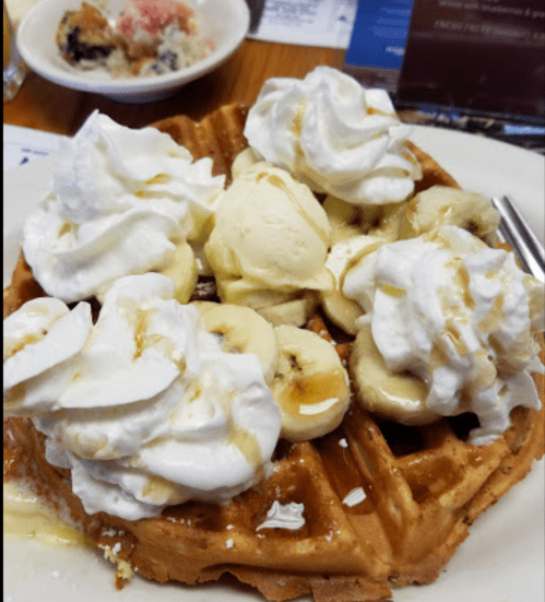 A delicious waffle topped with whipped cream, sliced bananas, and drizzled with syrup.