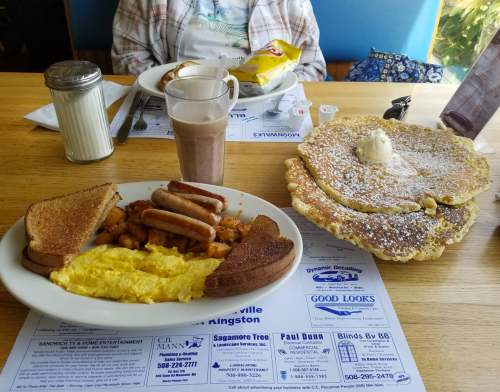 A hearty breakfast plate with eggs, sausage, hash browns, toast, and a large pancake with butter on the side.