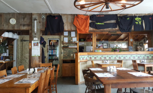 Cozy restaurant interior with wooden tables, chairs, and walls adorned with clothing and decor.