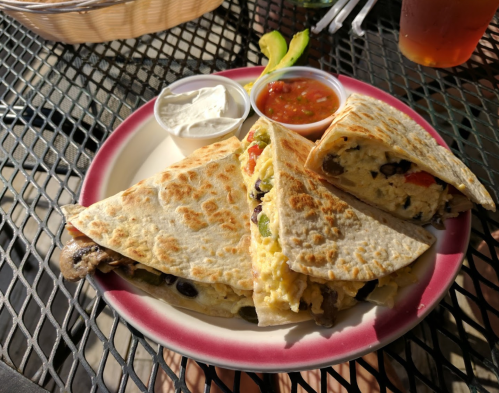A plate of quesadillas filled with vegetables, served with sour cream and salsa on a table.