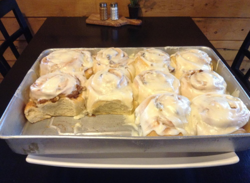 A tray of freshly baked cinnamon rolls topped with creamy icing, arranged neatly on a black table.