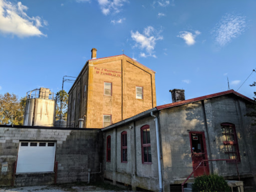 Historic building with a red roof, large windows, and a water tower, set against a blue sky with scattered clouds.