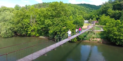 A suspension bridge over a river, surrounded by lush green trees and hills, with people walking across it.