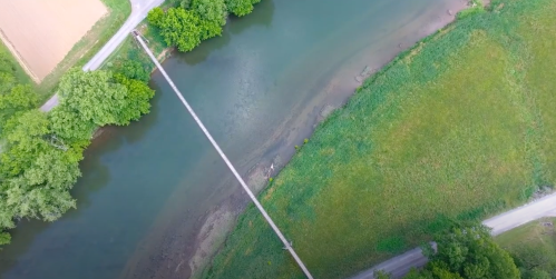 Aerial view of a river with a bridge, surrounded by green trees and grassy banks.