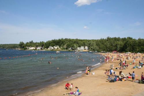 A busy beach scene with people swimming, sunbathing, and enjoying the sunny day by the water's edge.