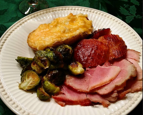 A plate of food featuring ham slices, roasted Brussels sprouts, and a cheesy potato dish.