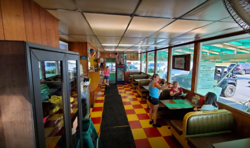 Interior of a diner with checkered floors, wooden walls, and patrons seated at booths. Bright and casual atmosphere.