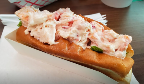 A lobster roll filled with creamy lobster salad on a toasted bun, garnished with a leaf of lettuce.