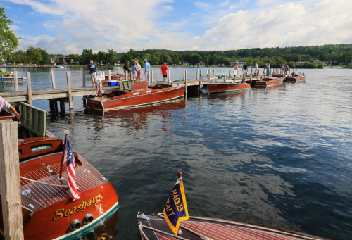 A scenic view of wooden boats docked at a pier on a calm lake, with people enjoying the waterfront.