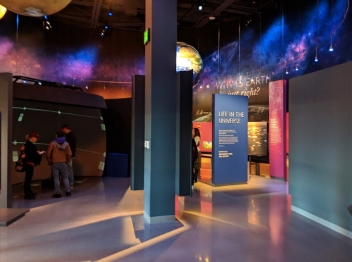 Interior of a science exhibit with colorful displays and visitors exploring various informational panels.