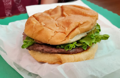 A hamburger with a beef patty, lettuce, and a soft bun, resting on white paper.