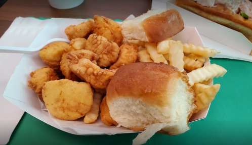 A tray of fried chicken pieces, crinkle-cut fries, and two soft bread rolls.