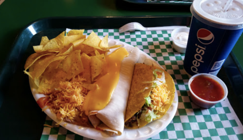 A tray with two tacos, cheese, shredded lettuce, nacho chips, salsa, and a Pepsi drink.