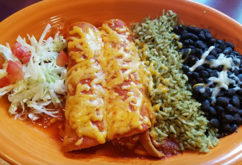 A vibrant plate featuring three cheese-covered enchiladas, rice, black beans, and a side of lettuce and tomato.
