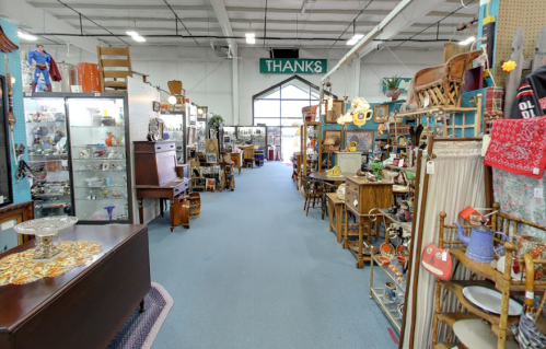 A spacious antique store aisle filled with various vintage items, furniture, and decor, leading to a bright entrance.