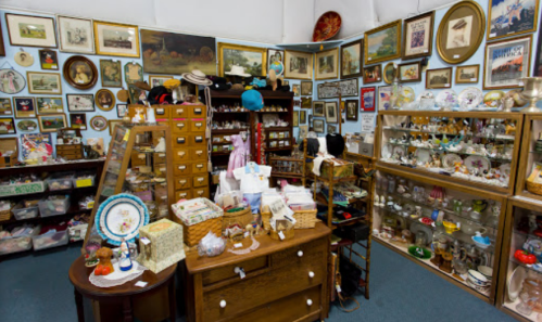 A cozy antique shop filled with various collectibles, framed art, and vintage items displayed on shelves and tables.