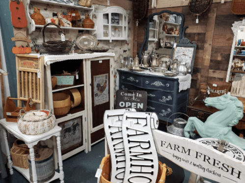 A cozy vintage shop filled with rustic decor, including furniture, baskets, and farm-themed signs.