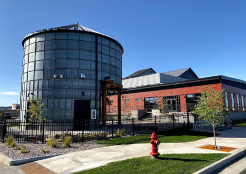 A modern building with a metal silo, red accents, and a landscaped area featuring a fire hydrant and bike racks.