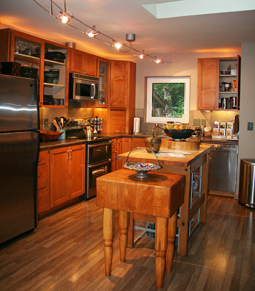 Modern kitchen with wooden cabinets, stainless steel appliances, and a central island with a bowl on top. Warm lighting.
