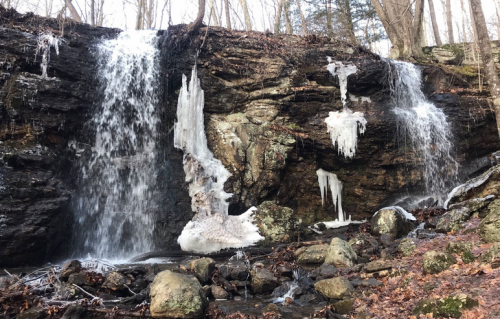 A serene waterfall cascading over rocky cliffs, surrounded by icicles and autumn leaves in a tranquil forest setting.