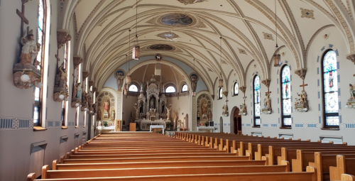 Interior of a church featuring wooden pews, ornate arches, stained glass windows, and religious statues.
