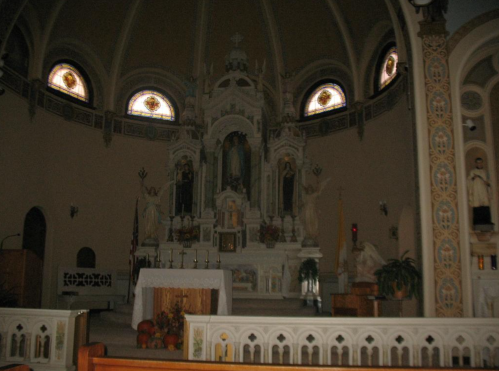 Interior of a church featuring an altar, stained glass windows, and ornate architectural details.