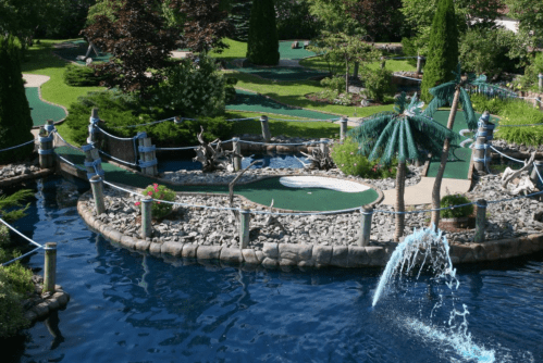 A scenic mini-golf course with lush greenery, water features, and decorative palm trees.