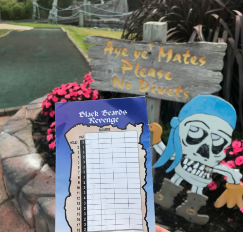 A scorecard for mini-golf titled "Black Beard's Revenge" in front of a whimsical pirate-themed sign.