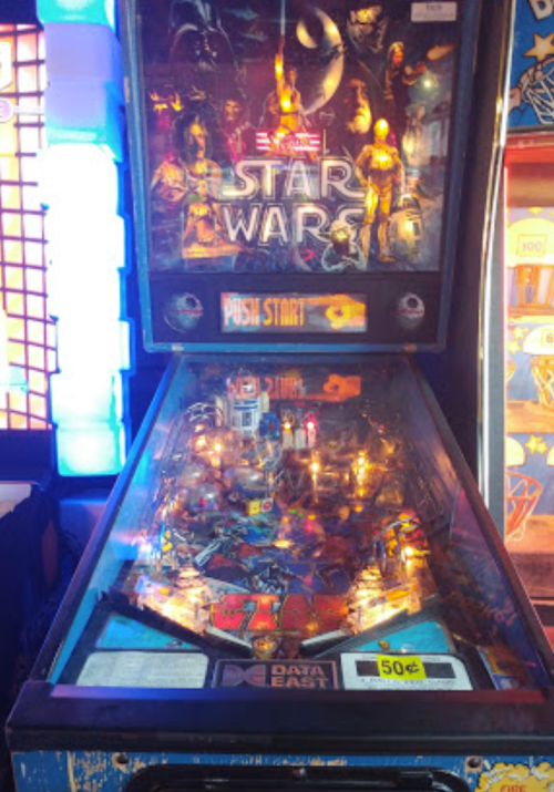 A Star Wars-themed pinball machine with vibrant artwork and illuminated playfield, set in an arcade.