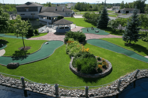 Aerial view of a mini-golf course with lush greenery, winding paths, and a gazebo in a scenic outdoor setting.