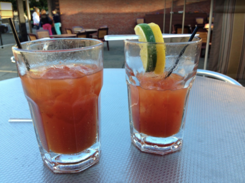 Two glasses of vibrant red cocktails with ice, garnished with lemon and lime slices, on a table.