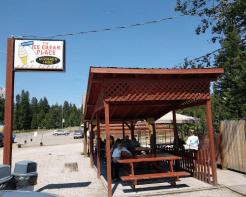A wooden outdoor seating area at an ice cream shop, with customers enjoying their treats under a sunny sky.