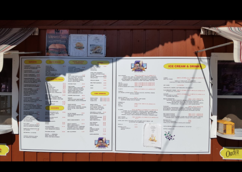 Menu board featuring ice cream, drinks, and food items with prices, displayed on a wooden wall.