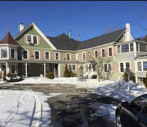 A large, multi-story green house with pink accents, surrounded by snow and a clear blue sky.
