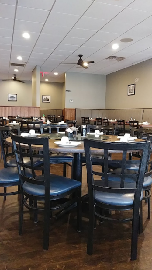 A spacious restaurant interior with empty tables and chairs, featuring a simple decor and ceiling fans.